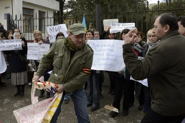 A man wearing a pro-Russia ribbon removes a placard during an anti-war picket in the Crimean city of Simferopol March 5, 2014. Russia said on Wednesday it could not order “self-defence” forces in Crimea back to their bases ahead of the first face-to-face talks with the United States on easing tensions over Ukraine and averting the risk of war. (Photo by Maks Levin/Reuters)