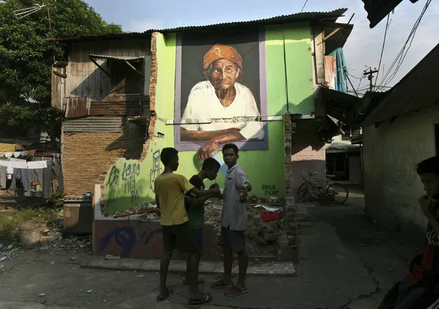 Indonesian youths share cold drinks near a mural depicting an elderly woman painted by British artist Gabriel Pitcher at a slum in Medan, North Sumatra, Indonesia, Thursday, March 9, 2017. (Photo by Binsar Bakkara/AP Photo)