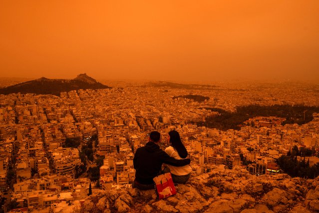 A couple sits on Tourkovounia hill, as southerly winds carry waves of Saharan dust, in Athens, on April 23, 2024. Clouds of dust blown in from the Sahara covered Athens and other Greek cities on April 23, 2024, one of the worst such episodes to hit the country since 2018, officials said. The yellow-orange haze smothered several regions, limiting visibility and prompting warnings of breathing risks from the authorities. (Photo by Angelos Tzortzinis/AFP Photo)