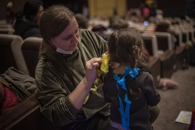 A woman ties ribbons in Ukrainian national flag colors in a girl's hair as people wait at the Metropolitan Assistance Centre for Ukrainian Refugees in the Congress Centre in Prague, Czech Republic, 07 March 2022. In total, Prague's center has registered almost 12.000 people since the beginning of the Russian invasion. According to estimates, roughly 100.000 refugees from Ukraine have arrived in the Czech Republic so far, the majority of them women, children and elderly people. (Photo by Martin Divisek/EPA/EFE)