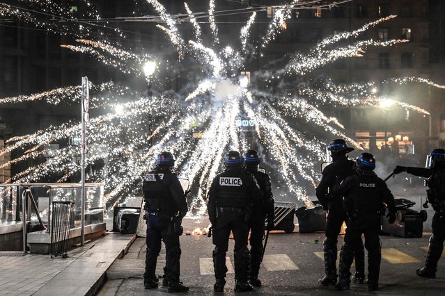 Police officers stand in fronf of fireworks fired by protesters during a demonstration after the French government pushed a pensions reform through parliament without a vote, using the article 49,3 of the constitution, in Lyon on March 16, 2023. The French president on March 16 rammed a controversial pension reform through parliament without a vote, deploying a rarely used constitutional power that risks inflaming protests. The move was an admission that his government lacked a majority in the National Assembly to pass the legislation to raise the retirement age from 62 to 64. (Photo by Olivier Chassignole/AFP Photo)