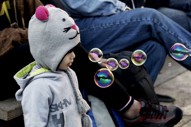 A migrant child watches bubble-blowing in Victoria Squares, where lots of migrants sleep rough, in central Athens, Greece, December 25, 2015. (Photo by Michalis Karagiannis/Reuters)