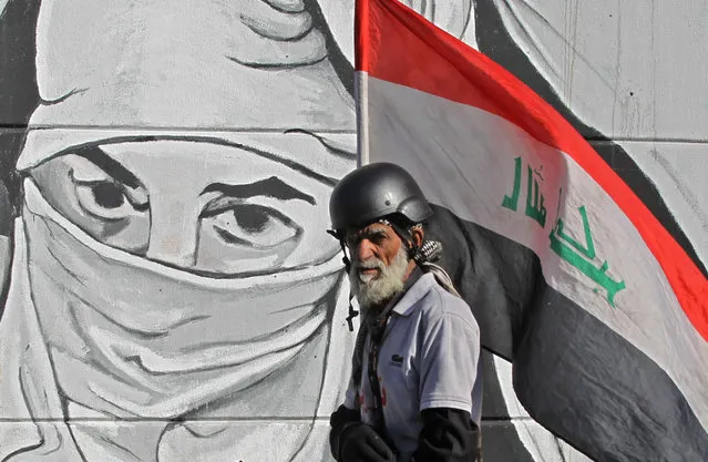 An Iraqi protester carrying his national flag walks past graffiti at Tahrir square in the capital Baghdad on December 20, 2019 during ongoing anti-government protests. Iraq's top Shiite cleric Grand Ayatollah Ali Sistani called today for early elections to end the months of political paralysis that have gripped the protest-hit country. “The quickest and most peaceful way out of the current crisis and to avoid plunging into the unknown, chaos or internal strife ... is to rely on the people by holding early elections”, said a representative of Sistani, who never appears in public. (Photo by Ahmad Al-Rubaye/AFP Photo)