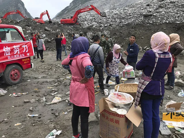 Women watch as earthmoving equipment digs at the site of a landslide in Xinmo village in Maoxian County in southwestern China's Sichuan Province, Sunday, June 25, 2017. (Photo by Ng Han Guan/AP Photo)