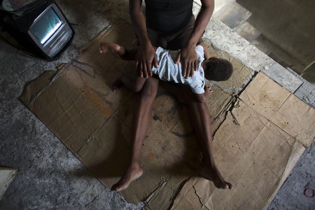 In this June 28, 2015 photo, Loavia Bienaime, 30, comforts her youngest daughter Martina as she watches TV in the stairwell outside their room in an abandoned earthquake-damaged government building in Port-au-Prince, Haiti. “I don't like the children here. It's very open. There is no security”, said Bienaime's husband, Jimmy Bellefleur. (Photo by Rebecca Blackwell/AP Photo)