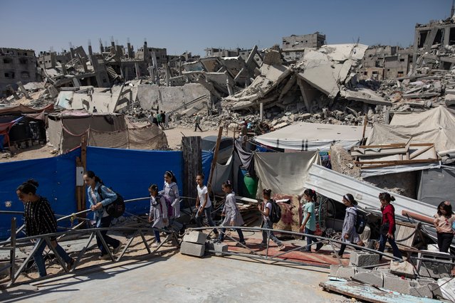 Palestinian children walk past destroyed buildings as they head to class in the Khan Younis camp, southern Gaza Strip, 12 September 2024. Palestinian teacher Israa Abu Mustafa (not pictured) set up a makeshift classroom in a tent built on the rubble of her old house. According to a statement released by the Palestinian Ministry of Education, more than 650,000 students in the Gaza Strip are being deprived of their right to education for the second academic year in a row. At least 84 percent of schools in the Gaza Strip ‘require full reconstruction or significant rehabilitation before schooling can resume’, the United Nations Children's Fund (UNICEF) reported in September 2024. More than 41,000 Palestinians and over 1,400 Israelis have been killed, according to the Palestinian Health Ministry and the Israel Defense Forces (IDF), since Hamas militants launched an attack against Israel from the Gaza Strip on 07 October 2023, and the Israeli operations in Gaza and the West Bank which followed it. (Photo by Haitham Imad/EPA/EFE)