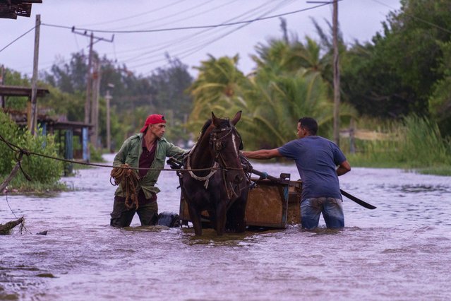 People traverse a flooded street with a horse-drawn carriage after the passage of Hurricane Helene in Guanimar, Artemisa province, Cuba, Wednesday, September 25, 2024. (Photo by Ramon Espinosa/AP Photo)