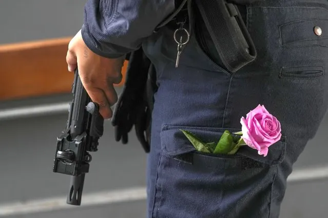 A police officer stands guard with a flower in his pocket as people gather to remember victims at the entrance of the Field's shopping center in Copenhagen, Denmark, Tuesday, July 5, 2022. Police say a gunman who killed three people when he opened fire in a crowded shopping mall acted alone and apparently selected his victims at random. They all but ruled out that Sunday's attack was related to terrorism. Authorities on Monday filed preliminary charges of murder and attempted murder against a 22-year-old Danish man. (Photo by Sergei Grits/AP Photo)