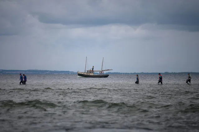 People walk through Puck Bay during the Herring March with a yacht in the background, in Kuznica, Poland August 19, 2017. (Photo by Jekaterina Saveljeva/Reuters)