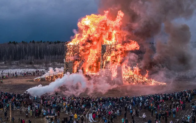 People watch a sculpture of a bridge burning at the Maslenitsa (Shrovetide) festival at the Nikola-Lenivets art park in Nikola-Lenivets village, about 200 kilometers (125 miles) south-west of Moscow, Russia, Saturday, February 29, 2020. Maslenitsa is a traditional Russian holiday marking the end of winter that dates back to the pagan times. (Photo by Dmitry Serebryakov/AP Photo)