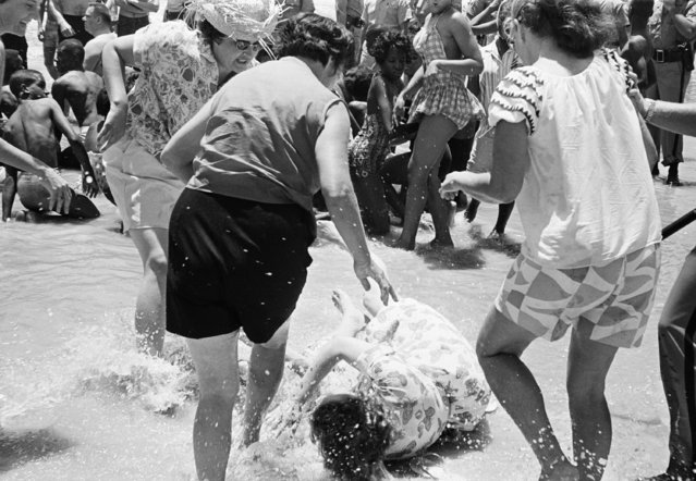 A woman falls to the beach after she was attacked by three white women segregationists, when she attempted a wade-in with several African American and white desegregationist demonstrators, June 23, 1964, St. Augustine Beach, Fla. The people in the photo are unidentified. (Photo by AP Photo/JK)