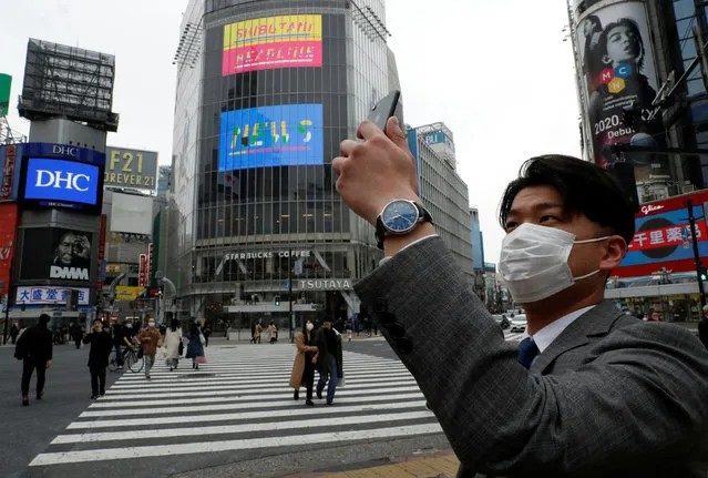 A man wearing a protective face mask, takes a photo with his mobile phone at noon, at Shibuya Crossing, during the coronavirus disease (COVID-19) outbreak, in Tokyo, Japan, March 31, 2020. (Photo by Issei Kato/Reuters)