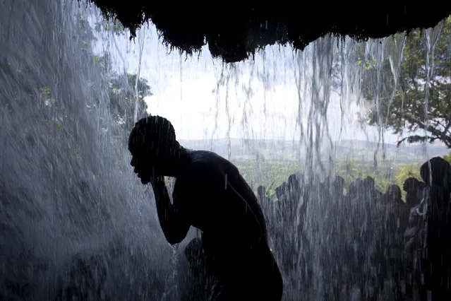 In this July 16, 2016 photo, a Voodoo pilgrim bathes in a waterfall believed to have purifying powers during the annual celebration in Saut d' Eau, Haiti. The area holds cultural significance to both Catholic and Voodoo practitioners. In the 19th century, it is believed that the Virgin Mary of Mount Carmel appeared on a palm tree there. (Photo by Dieu Nalio Chery/AP Photo)
