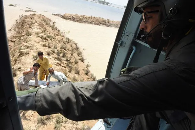 This aerial photograph taken on September 3, 2022 shows a Pakistan army soldier as he distributes relief tent and food bags from a helicopter to flood-affected people after heavy monsoon rains in Jaffarabad district, Balochistan province. Monsoon rains have submerged a third of Pakistan, claiming at least 1,190 lives since June and unleashing powerful floods that have washed away swathes of vital crops and damaged or destroyed more than a million homes. (Photo by Banaras Khan/AFP Photo)