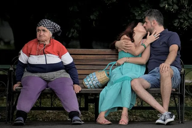 A couple kisses sitting on a bench next to an elderly woman in Bucharest, Romania, Thursday, June 30, 2022. (Photo by Vadim Ghirda/AP Photo)
