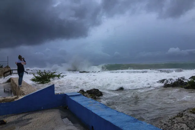 A woman takes photos while waves crash against a seawall as Hurricane Ian passes through George Town, Grand Cayman island, Monday, September 26, 2022. Hurricane Ian is on a track to hit the west coast of Florida as a major hurricane as early as Wednesday. (Photo by Kevin Morales/AP Photo)