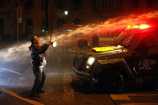 A demonstrator is hit by a stream of water from a police vehicle as Chilean riot police squads attempt to control a demonstration held by protestors demanding an end to the private retirement pension system that has been in place since the days of Augusto Pinochet's dictatorship in Santiago, Chile, 10 August 2016. (Photo by Sebastian Silva/EPA)