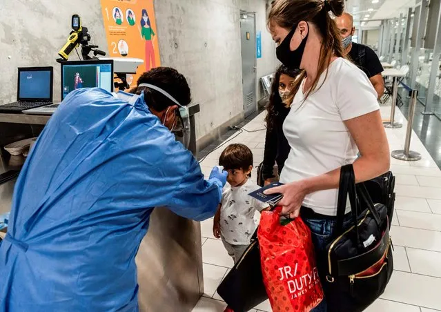 This picture taken on June 9, 2020 shows a health worker at Cyprus' Larnaca International Airport measuring the temperature of a child arriving woth other incoming travellers, as part of screening for symptoms of COVID-19 coronavirus disease. Cyprus opened back up for international tourism on June 9, with airports welcoming visitors after an almost three-month shutdown due to the COVID-19 coronavirus pandemic, with a bold plan to cover health care costs for visitors. (Photo by Iakovos Hatzistavrou/AFP Photo)
