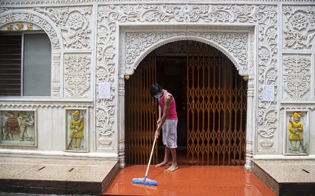 An Indian boy cleans the entrance area of a temple during the reimposed lockdown in Gauhati, India, Monday, June 29, 2020. India has reported a new daily record of nearly 20,000 new infections as several Indian states reimpose partial or full lockdowns to stem the spread of the coronavirus. (Photo by Anupam Nath/AP Photo)