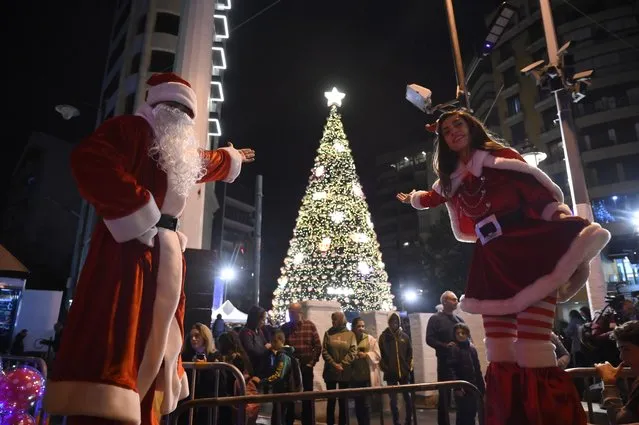 People dress as Santa Clauses pose in front of the 17-meter-high Christmas tree, which has been officially lit up at the Ashrafieh area in Beirut, Lebanon, 07 December 2022. (Photo by Wael Hamzeh/EPA/EFE)
