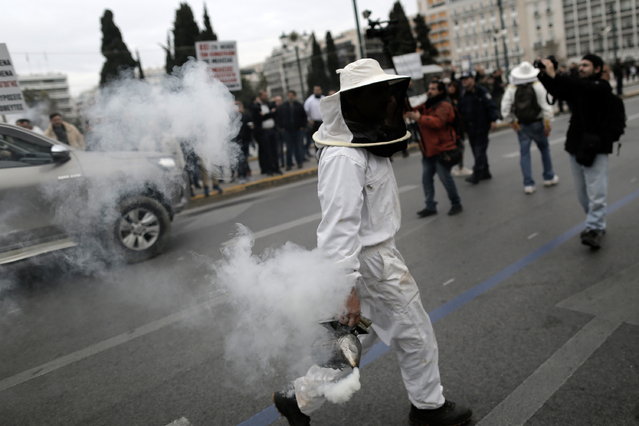 A beekeeper holding a smoker attends a rally of beekeepers in front of the Greek Parliament building in Athens, Greece, 22 February 2024. Beekeepers rally in Athens calling the Greek government to take steps to prevent imported honey from being sold as Greek and for assistance in tackling higher production costs. (Photo by Kostas Tsironis/EPA)