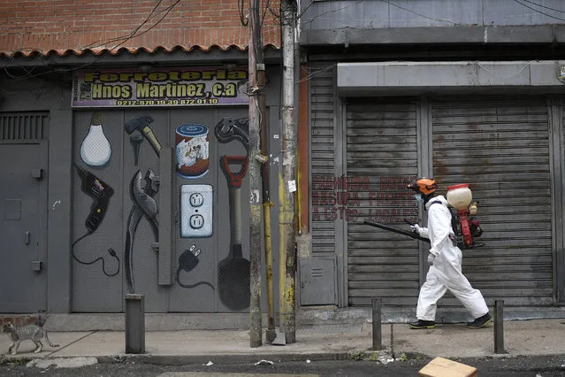 A city worker sprays disinfectant on shuttered storefronts in the Catia neighborhood of Caracas, Venezuela, Saturday, August 8, 2020, amid the new coronavirus pandemic. (Photo by Matias Delacroix/AP Photo)
