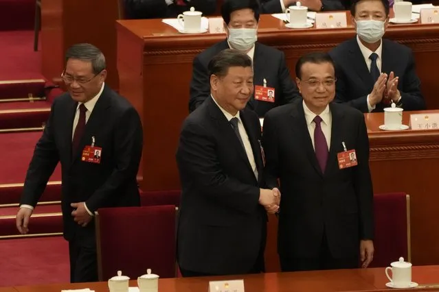 Newly elected Chinese Premier Li Qiang, at left, walks past as Chinese President Xi Jinping, center, shakes hands with former Premier Li Keqiang during a session of China's National People's Congress (NPC) at the Great Hall of the People in Beijing, Saturday, March 11, 2023. (Photo by Mark Schiefelbein/AP Photo)