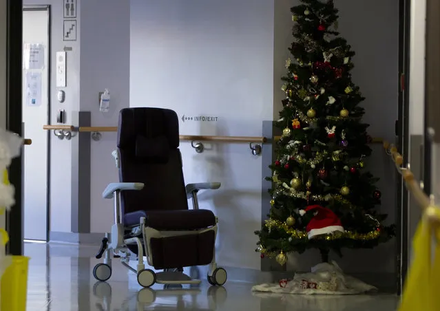 An empty chair is left in a hallway next to a Christmas tree in the COVID-19 ward at the St. Michiel Hospital in Brussels, Tuesday, November 24, 2020. Nations are struggling to reconcile cold medical advice with a holiday tradition that calls for big gatherings in often poorly ventilated rooms, where people chat, shout and sing together, providing an ideal conduit for a virus that has killed over 350,000 people in Europe so far. (Photo by Virginia Mayo/AP Photo)