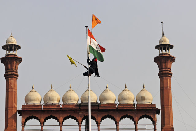 A Sikh man hangs on to a pole holding a Sikh religious flag along with a farm union flag at the historic Red Fort monument in New Delhi, India, Tuesday, January 26, 2021. Tens of thousands of protesting farmers drove long lines of tractors into India's capital on Tuesday, breaking through police barricades, defying tear gas and storming the historic Red Fort as the nation celebrated Republic Day. (Photo by Supreet Sapkal/AP Photo)
