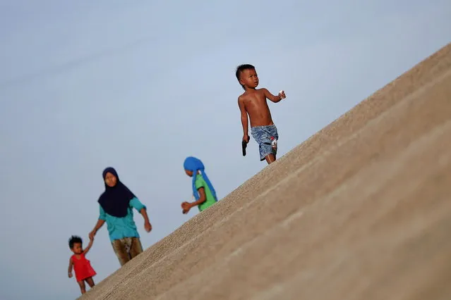 Ethnic Cham Muslim children walk on the banks of Tonle Sap river in Phnom Penh July 30, 2013. About 100 ethnic Cham families, made up of nomads and fishermen without houses or land who arrived at the Cambodian capital in search of better lives, live on their small boats on a peninsula where the Mekong and Tonle Sap rivers meet, just opposite the city's centre. The community has been forced to move several times from their locations in Phnom Penh as the land becomes more valuable. They fear that their current home, just behind a new luxurious hotel under construction at the Chroy Changva district is only temporary and that they would have to move again soon. (Photo by Damir Sagolj/Reuters)