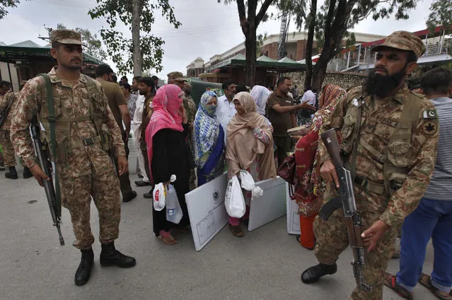 Pakistani troops stand guard while election staff wait for transport after collecting ballot boxes and polling material from a distribution center in Rawalpindi, Pakistan, Tuesday, July 24, 2018. As Pakistan prepares to make history Wednesday by electing a third straight civilian government, rights activists, analysts and candidates say the campaign has been among its dirtiest ever, imperiling the country's wobbly transition to democratic rule. (Photo by Anjum Naveed/AP Photo)