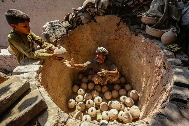 An Afghan boy helps a potter to sort clay piggy banks inside a kiln in Jalalabad on August 27, 2023. (Photo by Shafiullah Kakar/AFP Photo)