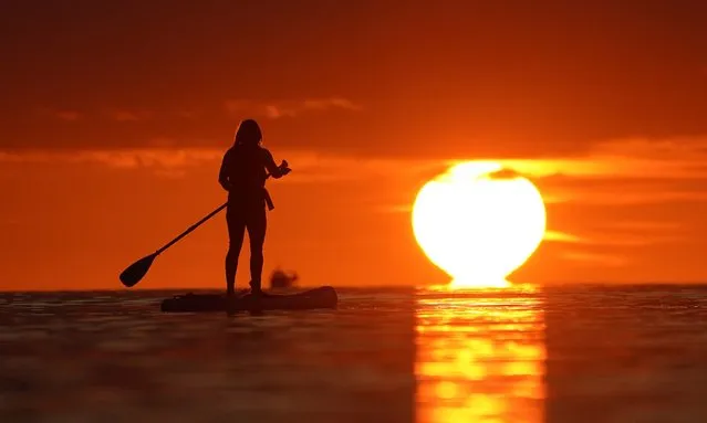 A paddleboarder makes her way out to sea during sunrise at Cullercoats Bay, North Tyneside, England on Friday, August 25, 2023. (Photo by Owen Humphreys/PA Images via Getty Images)