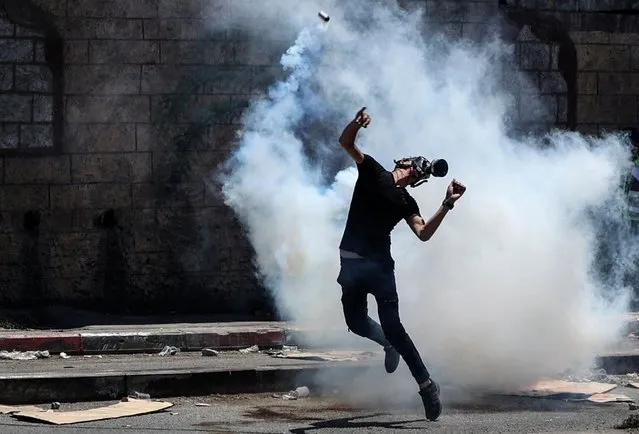 A Palestinian demonstrator returns a tear gas canister fired by Israeli security forces during clashes with them following a protest against Israeli settlements in the village of Beita near the occupied West Bank city of Nablus, on June 18, 2021. (Photo by Abbas Momani/AFP Photo)