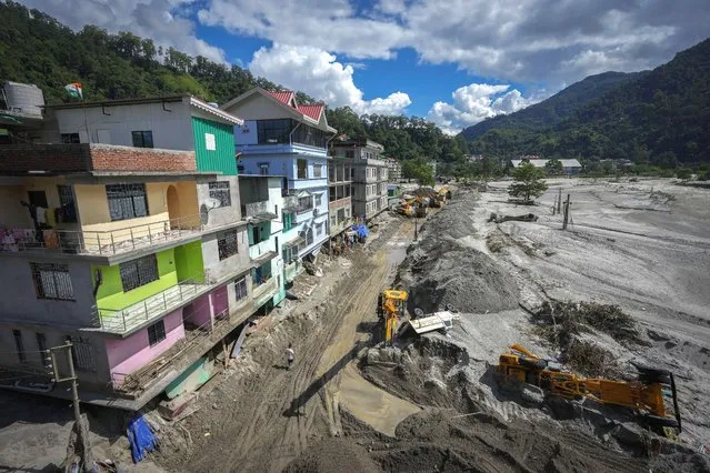 Vehicles that got washed away in floods lie on the sand as machinery is used to clean mud and sand near the buildings along the Teesta river in Rongpo, east Sikkim, India, Sunday, October. 8. 2023. Rescuers continued to dig through slushy debris and ice-cold water in a hunt for survivors after a glacial lake burst through a dam in India’s Himalayan northeast, shortly after midnight Wednesday, washing away houses and bridges and forcing thousands to flee. (Photo by Anupam Nath/AP Photo)