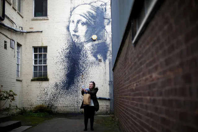 A woman photographs herself with a piece of street art attributed to Banksy titled “The Girl with the Pierced Eardrum” after it was defaced in an alleyway in Bristol, western England, October 22, 2014. (Photo by Andrew Winning/Reuters)