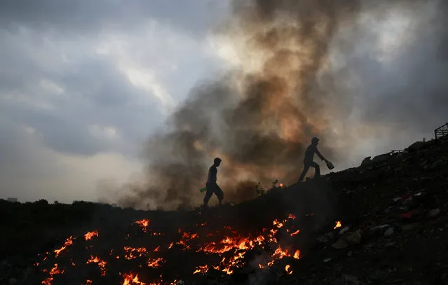 Impoverished Indians walk next to burning trash after relieving themselves in the open at Dharavi, one of the world's largest slums, in Mumbai, India, Thursday, April 9, 2015. Air pollution kills millions of people every year, including more than 627,000 in India, according to the World Health Organization. The WHO puts 13 Indian cities in the world's 20 most polluted. (Photo by Rafiq Maqbool/AP Photo)