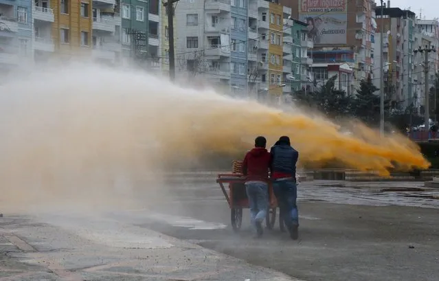 Street vendors take cover as Turkish riot police use a water cannon to disperse Kurdish demonstrators during a protest against the curfew in Sur district, in the southeastern city of Diyarbakir, Turkey, February 21, 2016. (Photo by Sertac Kayar/Reuters)
