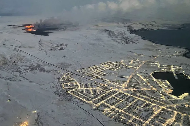 The evacuated Icelandic town of Grindavik (R) is seen as smoke billow and lava is thrown into the air from a fissure during a volcanic eruption on the Reykjanes peninsula 3 km north of Grindavik, western Iceland on December 19, 2023. A volcanic eruption began on Monday night in Iceland, south of the capital Reykjavik, following an earthquake swarm, Iceland's Meteorological Office reported. (Photo by Viken Kantarci/AFP Photo)