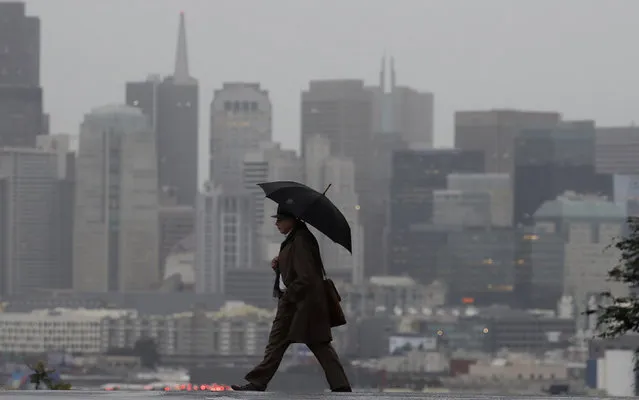 A man carries an umbrella as he crosses the street with the skyline at rear in San Francisco, Friday, February 1, 2019. A powerful storm bearing down on California on Friday was expected to produce heavy rainfall, damaging winds, localized stream flooding and heavy snow in the Sierra Nevada, forecasters said. (Photo by Jeff Chiu/AP Photo)