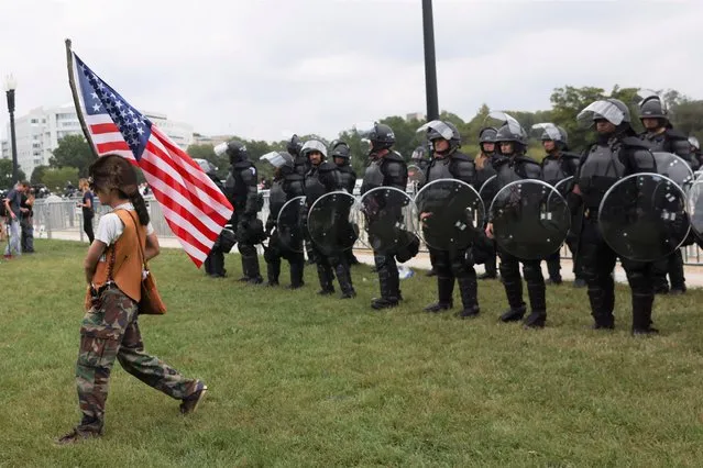 A demonstrator carrying a U.S flag passes by police officers standing in formation during a rally in support of defendants being prosecuted in the January 6 attack on the U.S. Capitol, in Washington, D.C., U.S., September 18, 2021. (Photo by Leah Millis/Reuters)
