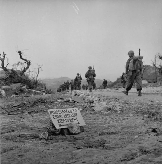 US Marines march past sign reading “ROAD EXPOSED TO ENEMY ARTILLERY, KEEP TO RIGHT” on their way towards the front lines during the fight to take Okinawa, 1945. (Photo by W. Eugene Smith/The LIFE Picture Collection/Getty Images)