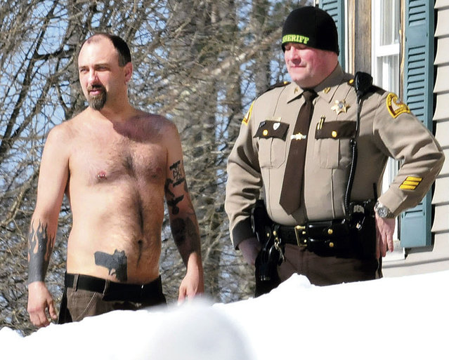 In this Tuesday, March 18, 2014 photo, Michael Smith, left, stands beside a Somerset County Sheriff deputy outside his home in Norridgewock, Maine. Officers armed with assault rifles descended on Smith's home after members of a tree removal crew he'd told to clear off his property reported that he had a gun. The “gun” the tree crew had seen on Smith actually was a life-sized tattoo of a handgun on his stomach. (Photo by David Leaming/AP Photo/Morning Sentinel)