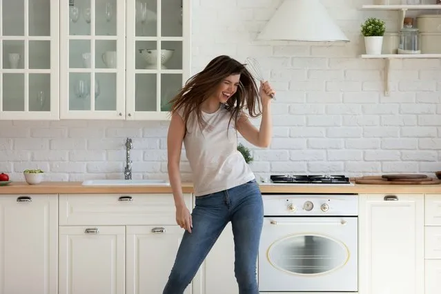 Happy young woman dancing alone having fun in modern living room in kitchen. Smiling female enjoying while cooking holding whisk, moving to favorite music enjoying weekend at home. (Photo by fizkes/Getty Images)