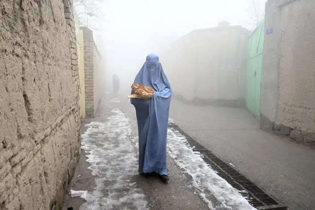 A woman wearing a burqa walks along a road towards her home after receiving free bread distributed as part of the Save Afghans From Hunger campaign in Kabul on January 18, 2022. (Photo by Wakil Kohsar/AFP Photo)