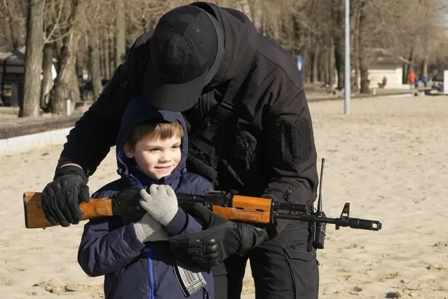 A member of a Ukrainian far-right group helps a boy to hold a Kalashnikov assault rifle during a training in Kyiv, Ukraine, Sunday, February 13, 2022. Russia denies it intends to invade but has massed well over 100,000 troops near the Ukrainian border and has sent troops to exercises in neighboring Belarus, encircling Ukraine on three sides. U.S. officials say Russia's buildup of firepower has reached the point where it could invade on short notice. (Photo by Efrem Lukatsky/AP Photo)