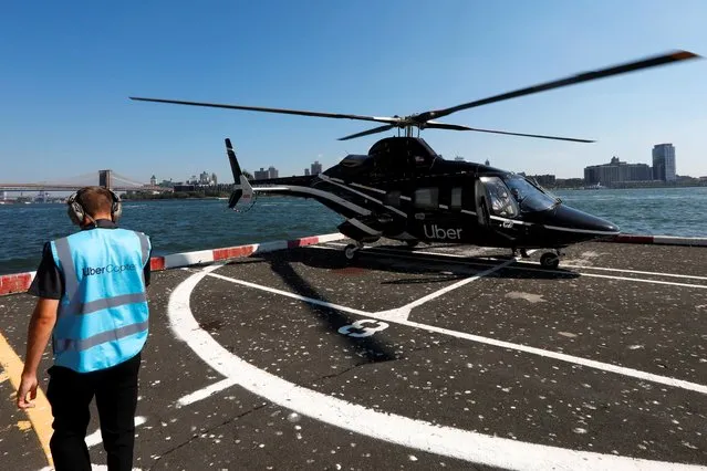 A worker walks media members to a waiting helicopter operated by Uber Copter, a new service by the ride-sharing company Uber, providing service from Manhattan to New York's JFK International Airport initially for Diamond and Platinum Uber Rewards members as well as special Uber partners in Manhattan, New York, U.S., October 2, 2019. Picture taken October 2, 2019. (Photo by Mike Segar/Reuters)