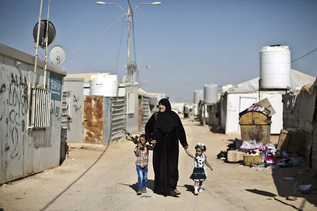 Syrian refugee children dressed in new clothes hold the hands of their grandmother while walking back to their shelter on the first day of the Eid al-Fitr holiday that marks the end of the holy fasting month of Ramadan at Zaatari refugee camp, in Mafraq, Jordan, Friday, July 17, 2015. (Photo by Muhammed Muheisen/AP Photo)