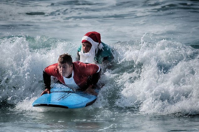 Mark Gabriel, right, dressed as Santa Claus, helps surfer Creighton Wall who suffers from Down Syndrome during the Surfing Santa event in Dana Point, Calif. on Sunday, December 8, 2024. (Photo by Richard Vogel/AP Photo)