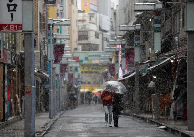 A scouple wearing protective face mask, following an outbreak of the coronavirus disease (COVID-19), walks on a nearly empty stree in a snow fall during the first weekend after Tokyo Governor Yuriko Koike (not in picture) urged Tokyo residents to stay indoors in a bid to keep the coronavirus disease (COVID-19) from spreading, at Ameyoko shopping and amusement district in Tokyo, Japan March 29, 2020. (Photo by Issei Kato/Reuters)